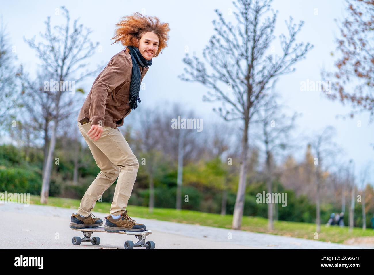 Skater mit lockigen rothaarigen Haaren auf einem Brett in einem Stadtpark Stockfoto