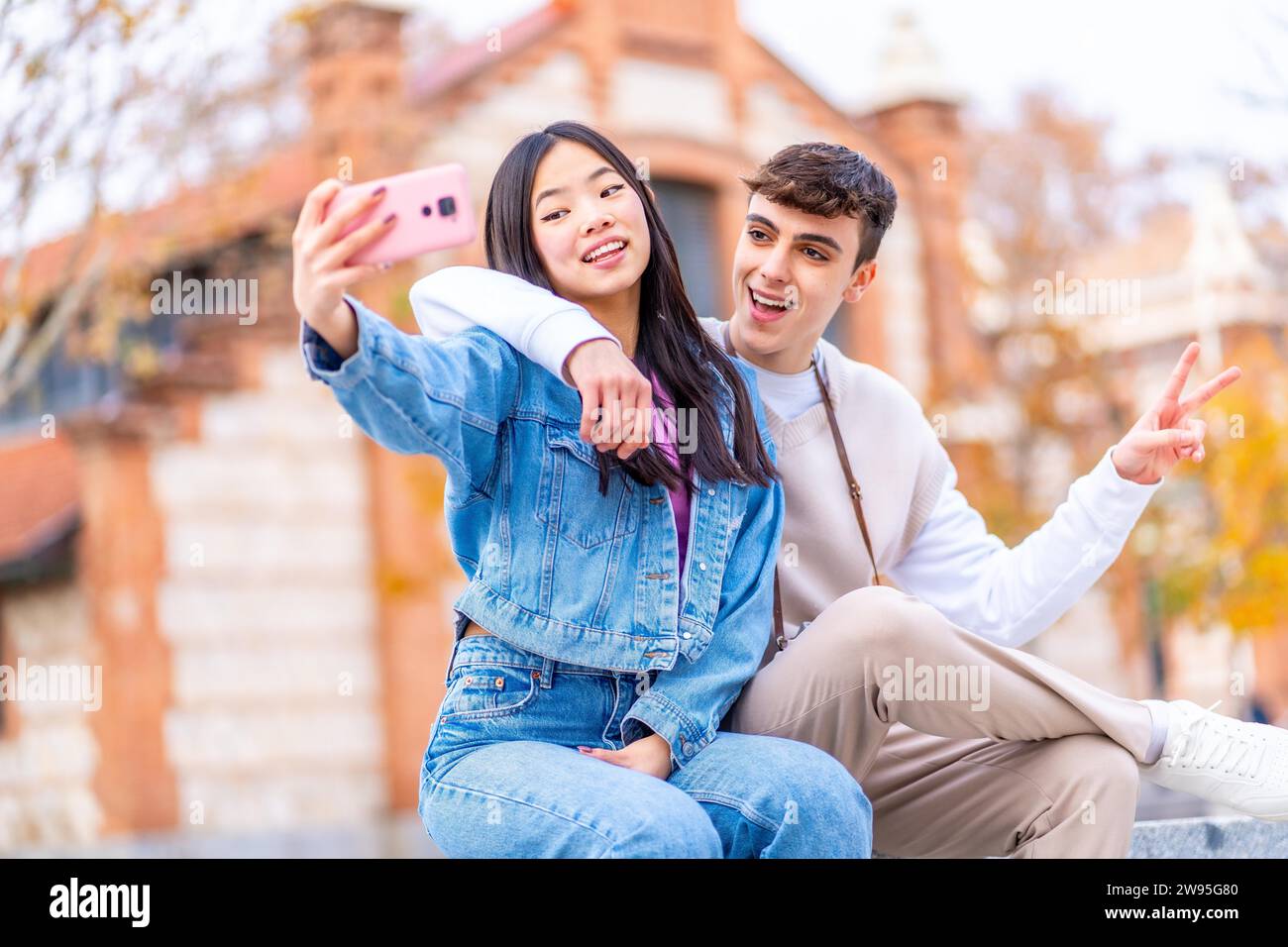Fröhliches Multi-ethnisches Paar, das ein Selfie macht, während das Handy auf der Straße sitzt Stockfoto