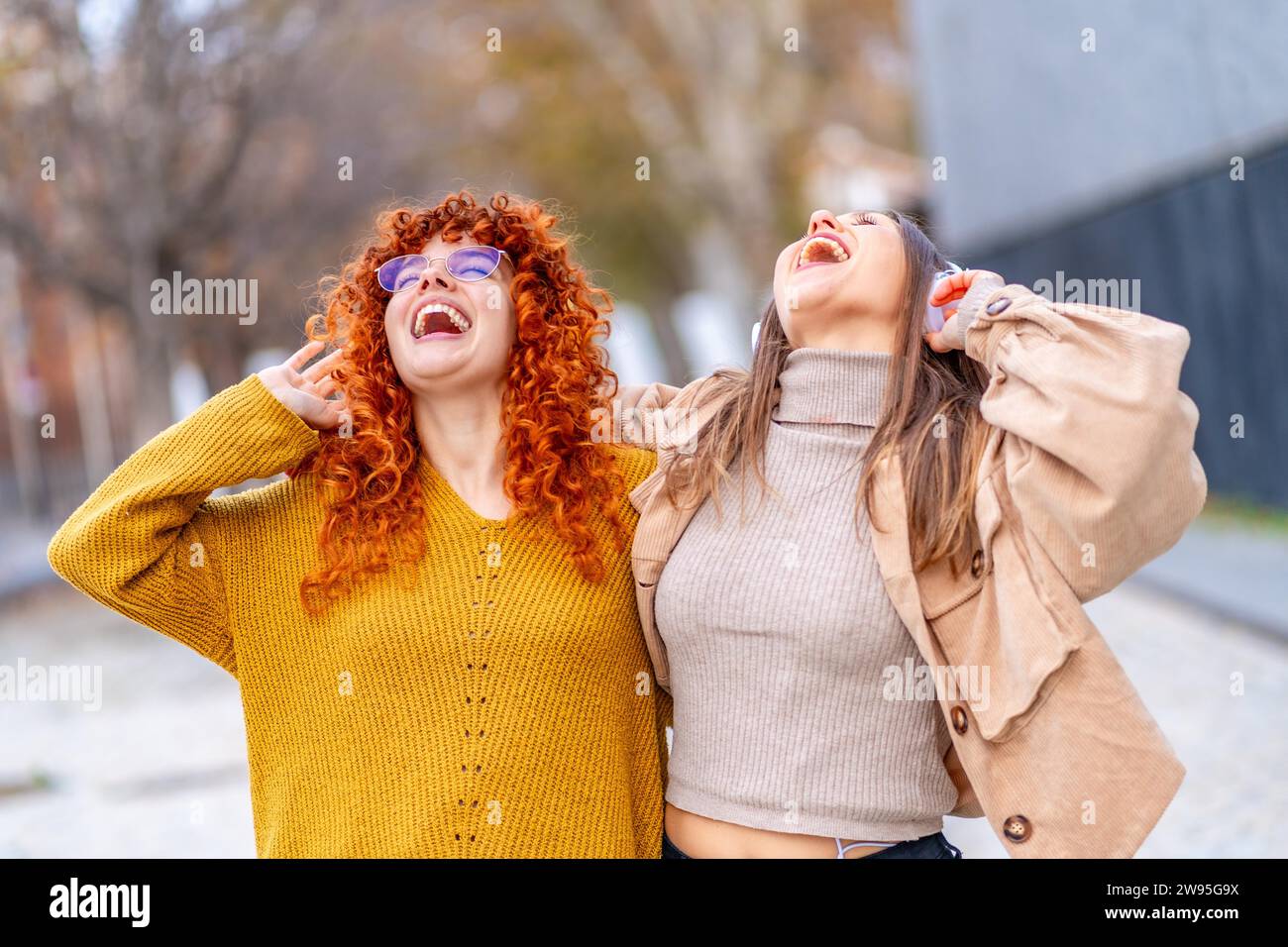 Frontporträt zweier aufgeregter Frauen, die draußen mit Kopfhörern singen und Musik hören Stockfoto