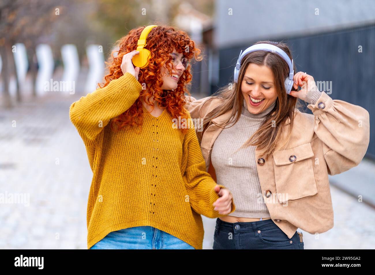 Frontalansicht zweier glücklicher Frauen, die auf der Straße tanzen und Musik hören Stockfoto