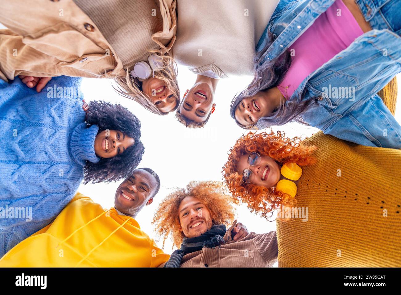 Niedriger Blickwinkel von multiethnischen Menschen, die einen Kreis bilden und in die Kamera lächeln Stockfoto