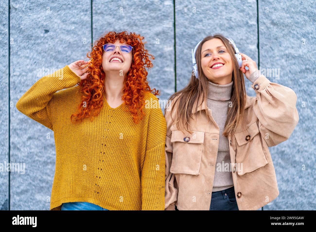 Frontporträt zweier glücklicher Frauen, die Musik hören, während Kopfhörer in der Stadt stehen Stockfoto