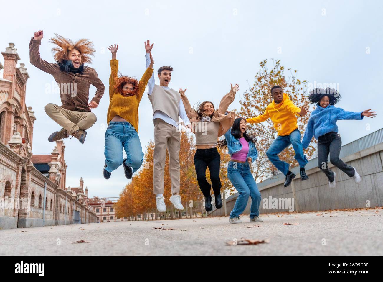 Glückliche, multiethnische Freunde, die an einem Herbsttag auf die Straße springen Stockfoto