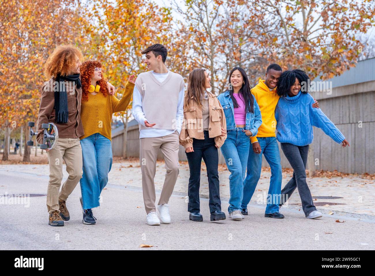 An einem Herbsttag plaudern und schlendern multiethnische Freunde entspannt entlang der Straße Stockfoto