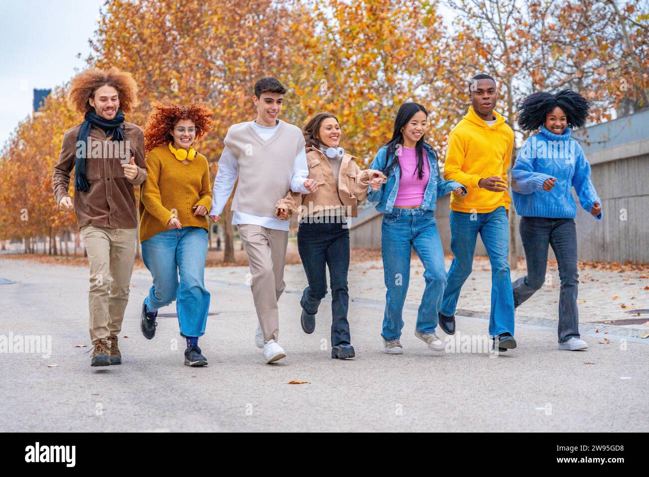 Weite Sicht auf verspielte Freunde aus verschiedenen Ethnien, die auf einer Straße laufen Stockfoto