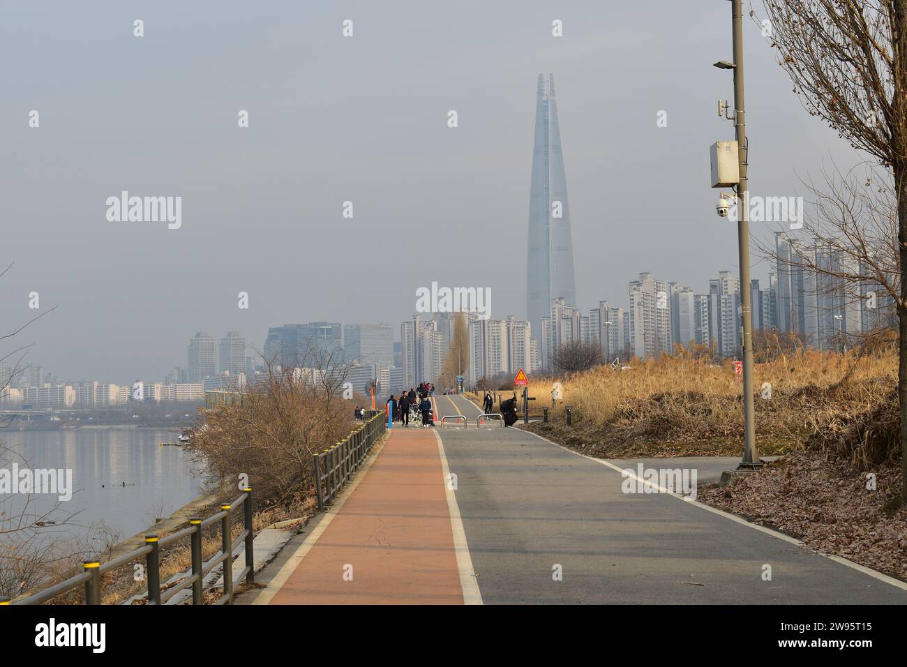 Blick auf einen Fußgänger- und Fahrradweg im Jamsil Hangang Park mit dem majestätischen Wolkenkratzer Lotte World Tower im Hintergrund Stockfoto