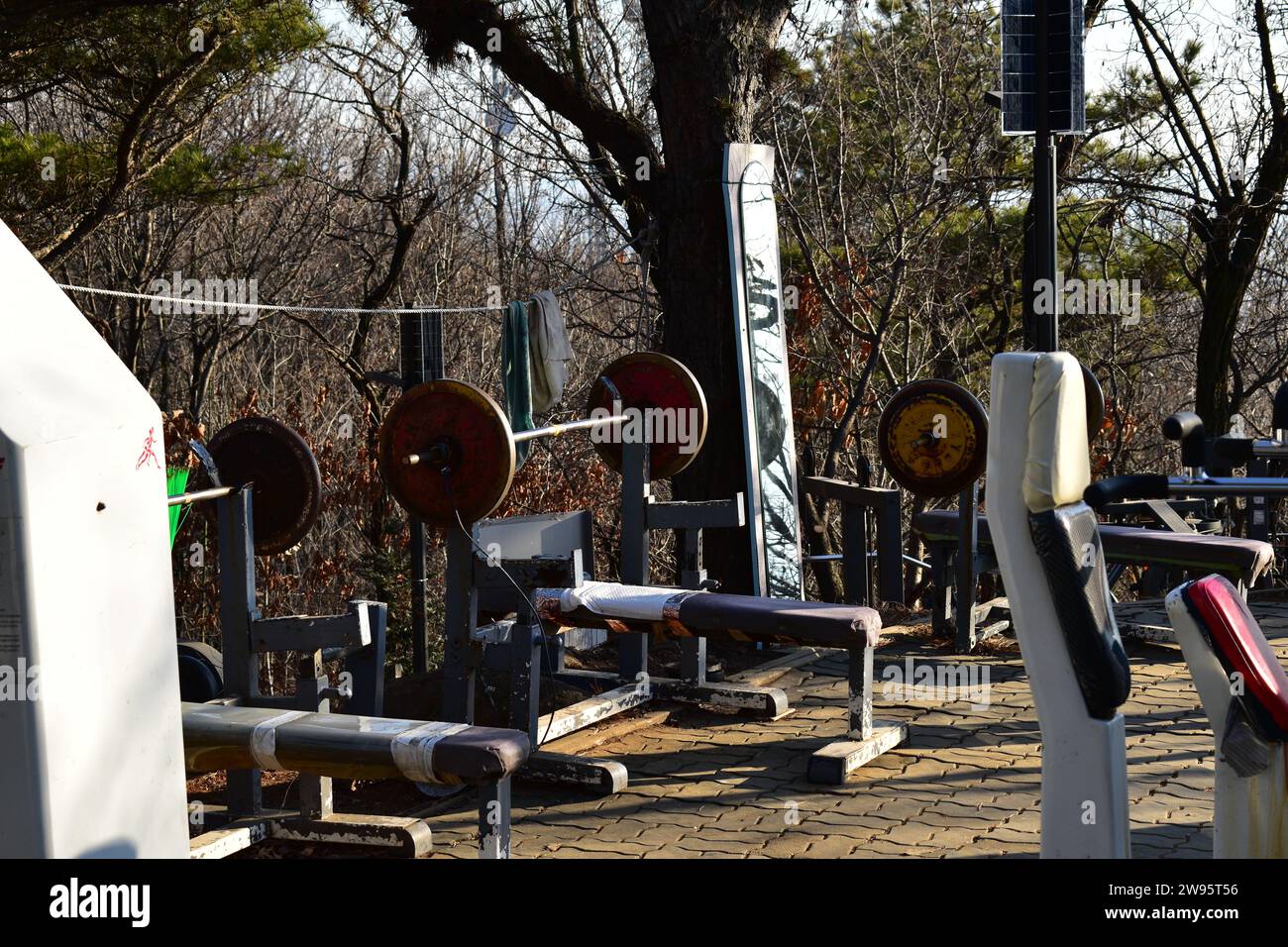 Öffentliche Bankpresse im Freien mit Langhantel und Gewichten und anderen Fitnessgeräten im Baengnyeon Neighborhood Park während Sonnenuntergang Stockfoto