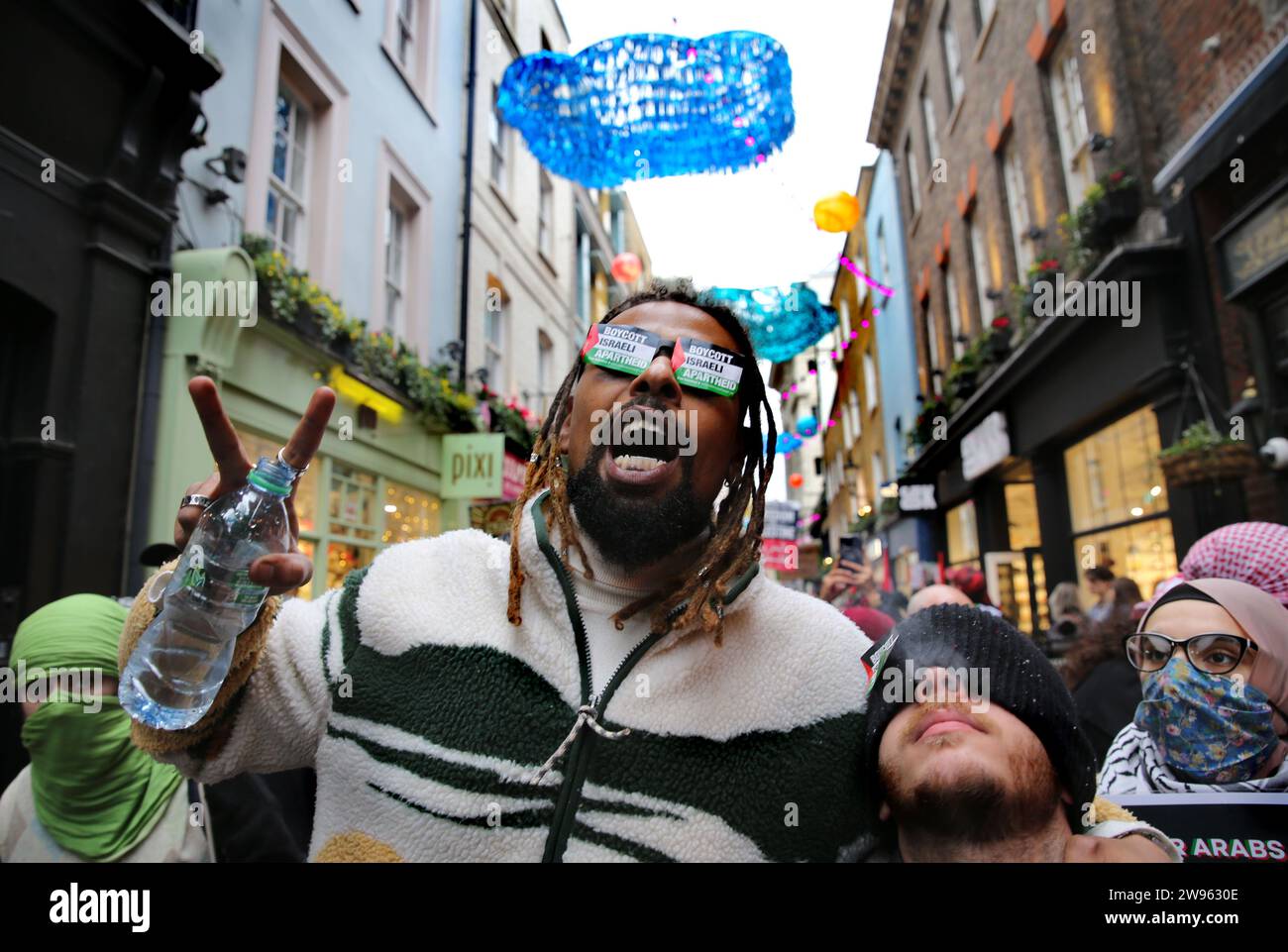 Ein Demonstrant trägt eine Brille mit Aufklebern auf beiden Gläsern, die während der Demonstration „die israelische Apartheid boykottieren“. Schwestern Unbeschnittene Unterstützer versammelten sich und marschierten im Londoner West End Einkaufsviertel zur Unterstützung der Palästinenser. Sie verlangten einen dauerhaften Waffenstillstand in Gaza und Kunden, Unternehmen zu boykottieren, die Israel unterstützen. Stockfoto