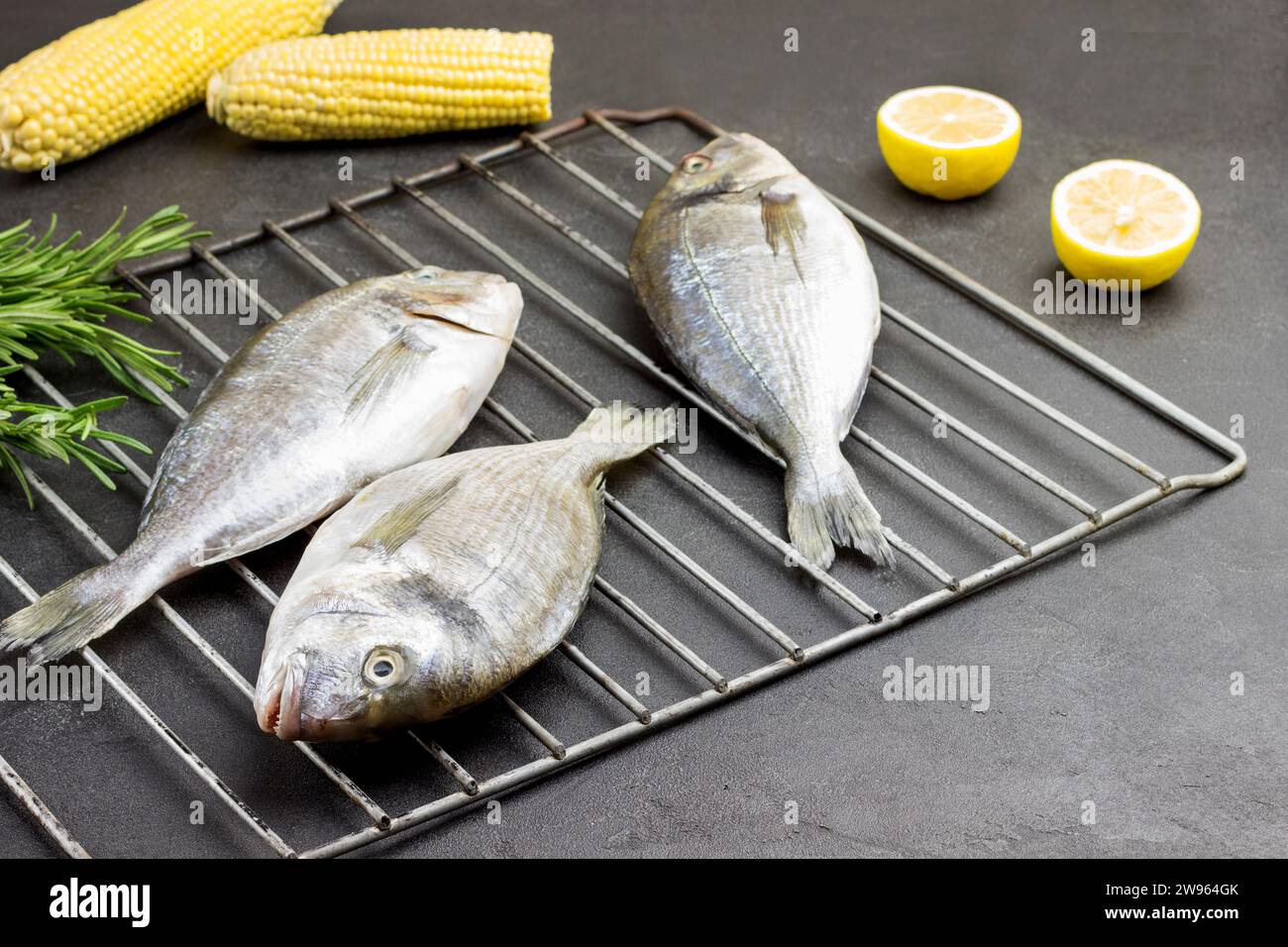 Frischer dorado-Fisch auf Metallgrill. Maiskolben und Zitrone. Schwarzer Hintergrund. Blick von oben Stockfoto