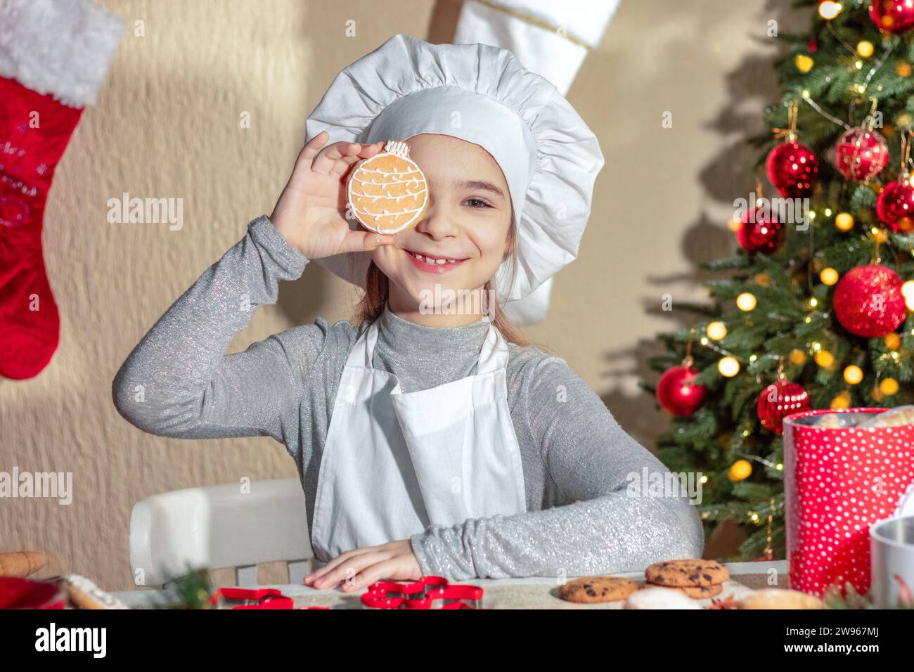 Fröhliches Mädchen schließt ihr Auge mit Weihnachtskuchenkeksen in Form einer Kugel Stockfoto