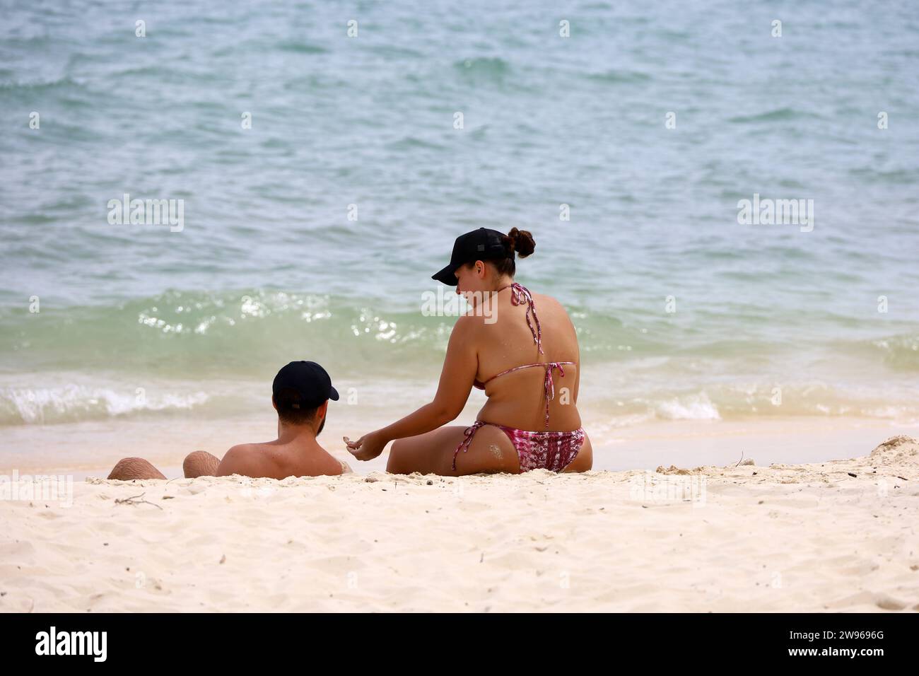 Verliebte Paare sitzen am Sandstrand vor den Meereswellen. Mann und Frau zusammen, romantische Freizeit an der Küste Stockfoto