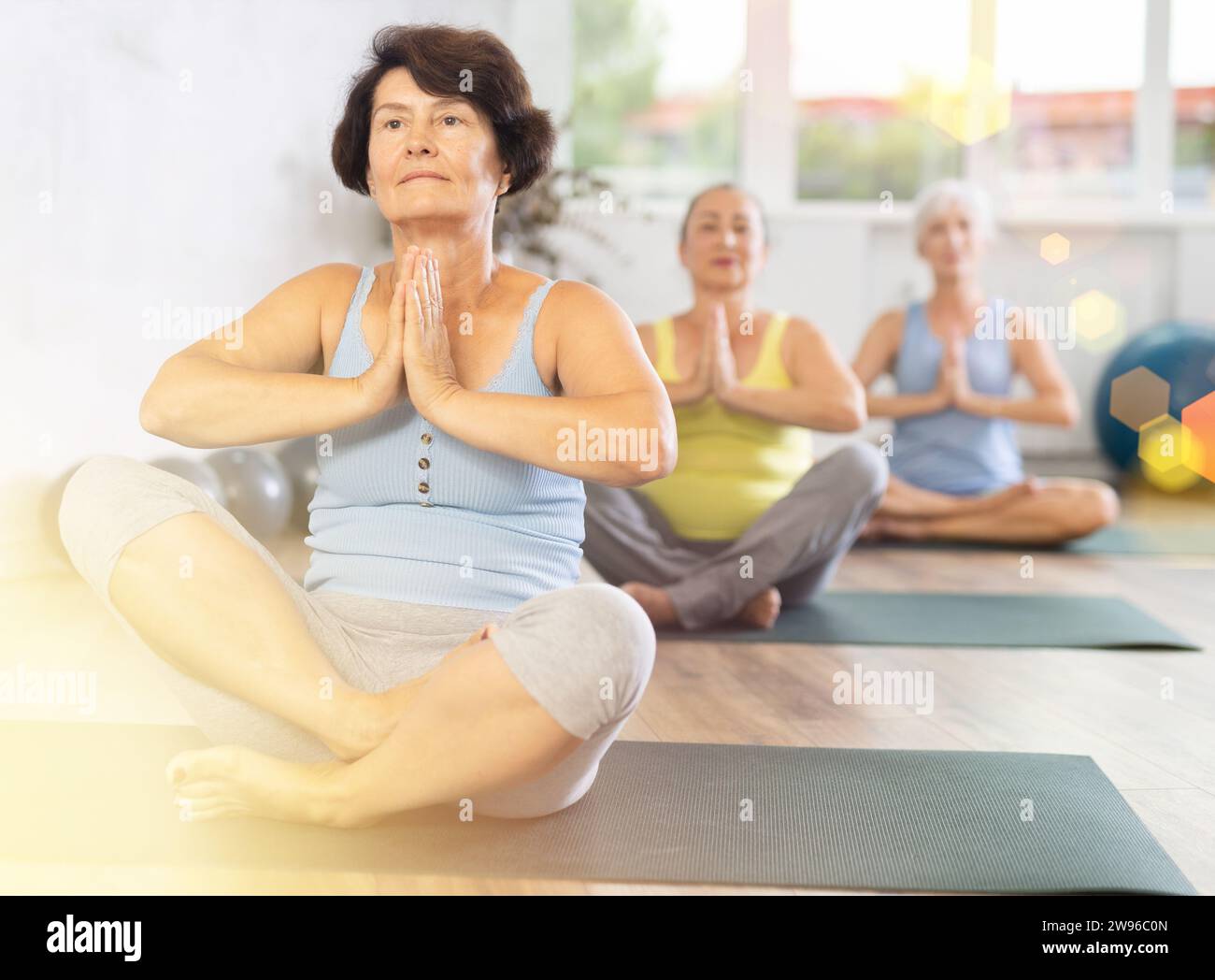Es gibt eine Gruppe Pilates-Klasse im Studio für Menschen unterschiedlichen Alters. Ältere Frauen in Begleitung von Hatha-Yoga-Liebhabern spielen Halb-Lotus-Pose, Ardha Pad Stockfoto
