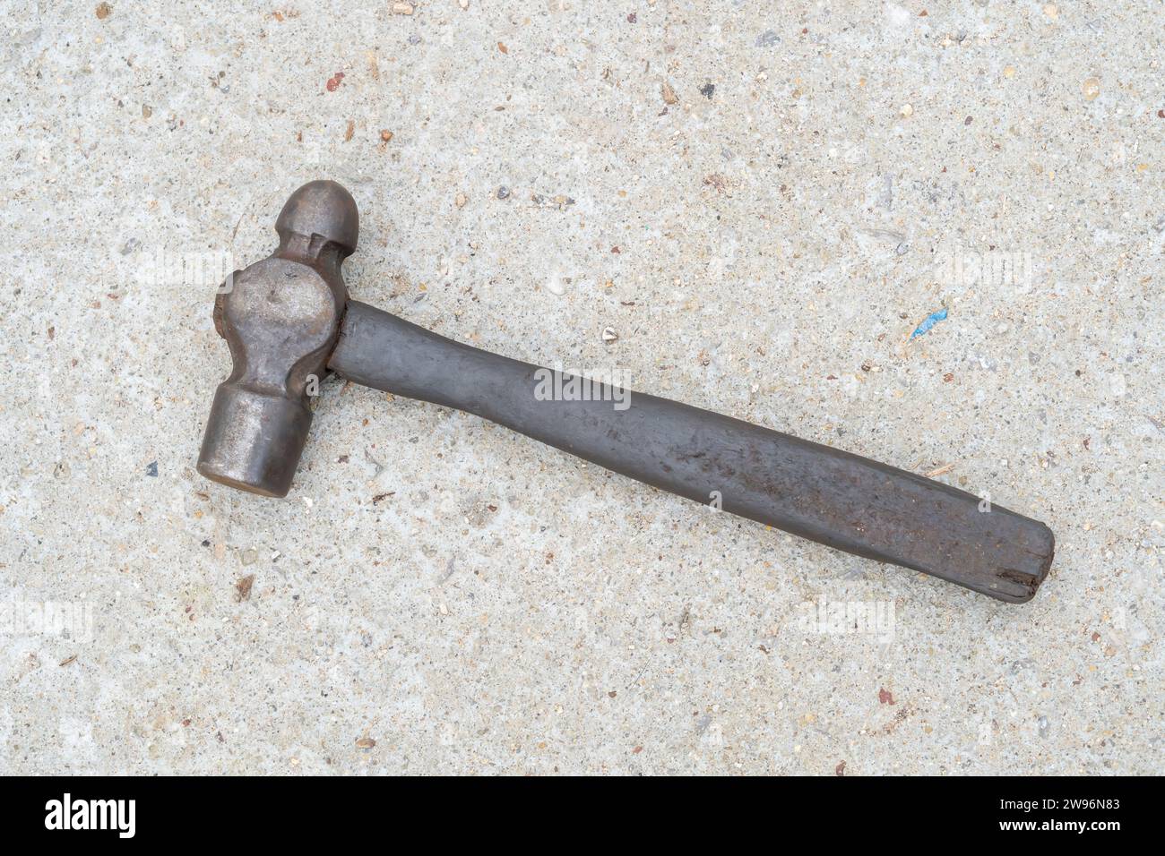 Ein einziger schmutziger alter Metall- oder Eisenhammer mit Holzgriff liegt auf Betonboden. Flache Lagen Stockfoto