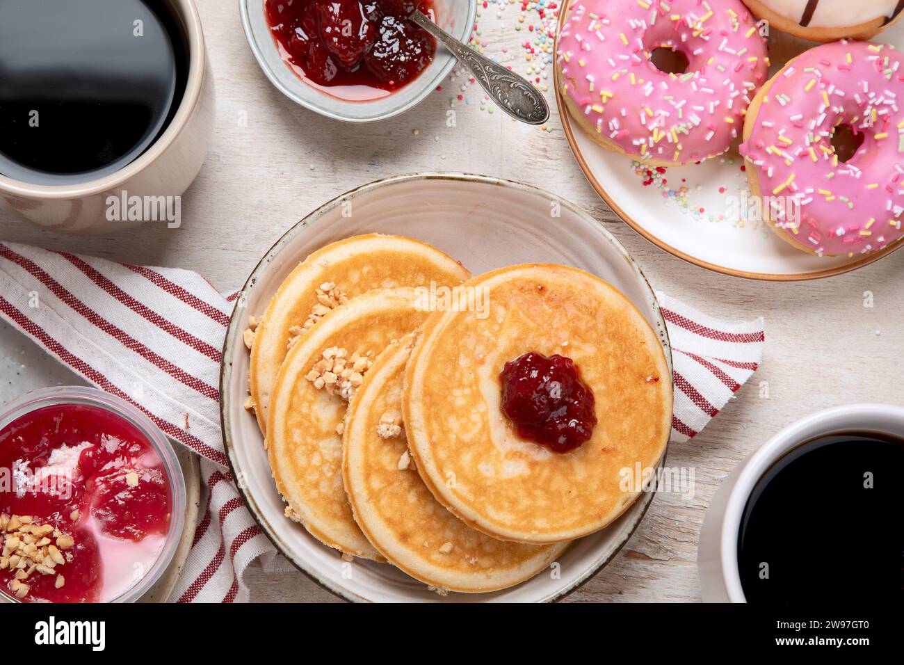 Tisch mit verschiedenen amerikanischen Keksen, Donuts, Pfannkuchen und Kaffeetassen auf weißem Hintergrund. Draufsicht. Stockfoto