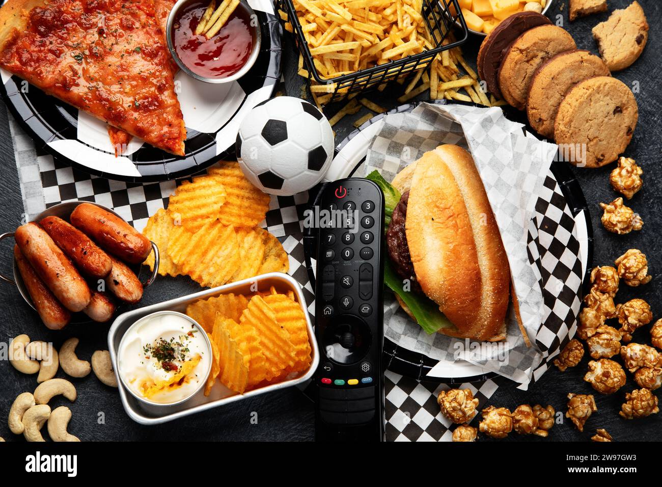 Gesättigte Fette. Fußballzeit. TV-Fernbedienung und Snacks - Chips, Popcorn, Kekse, Käse, Soße, Pommes, Burger, Nüsse. Draufsicht Stockfoto