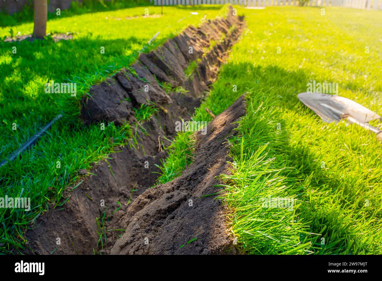 Ein Graben, der im Rasen gegraben wurde, um Rohre zu verlegen und Bewässerung zu installieren. Boden unter grünem Rasen und Graswurzelsystem Stockfoto