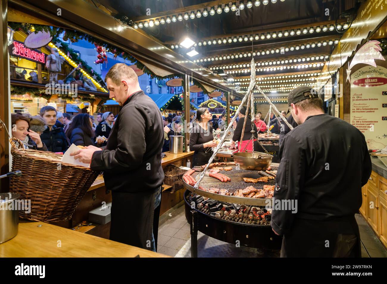 Bonn, Deutschland - 16. Dezember 2023 : Blick auf einen Imbissstand mit einem riesigen Barbecue, der verschiedene deutsche Würstchen und Steaks auf dem Weihnachtsmarkt in bietet Stockfoto