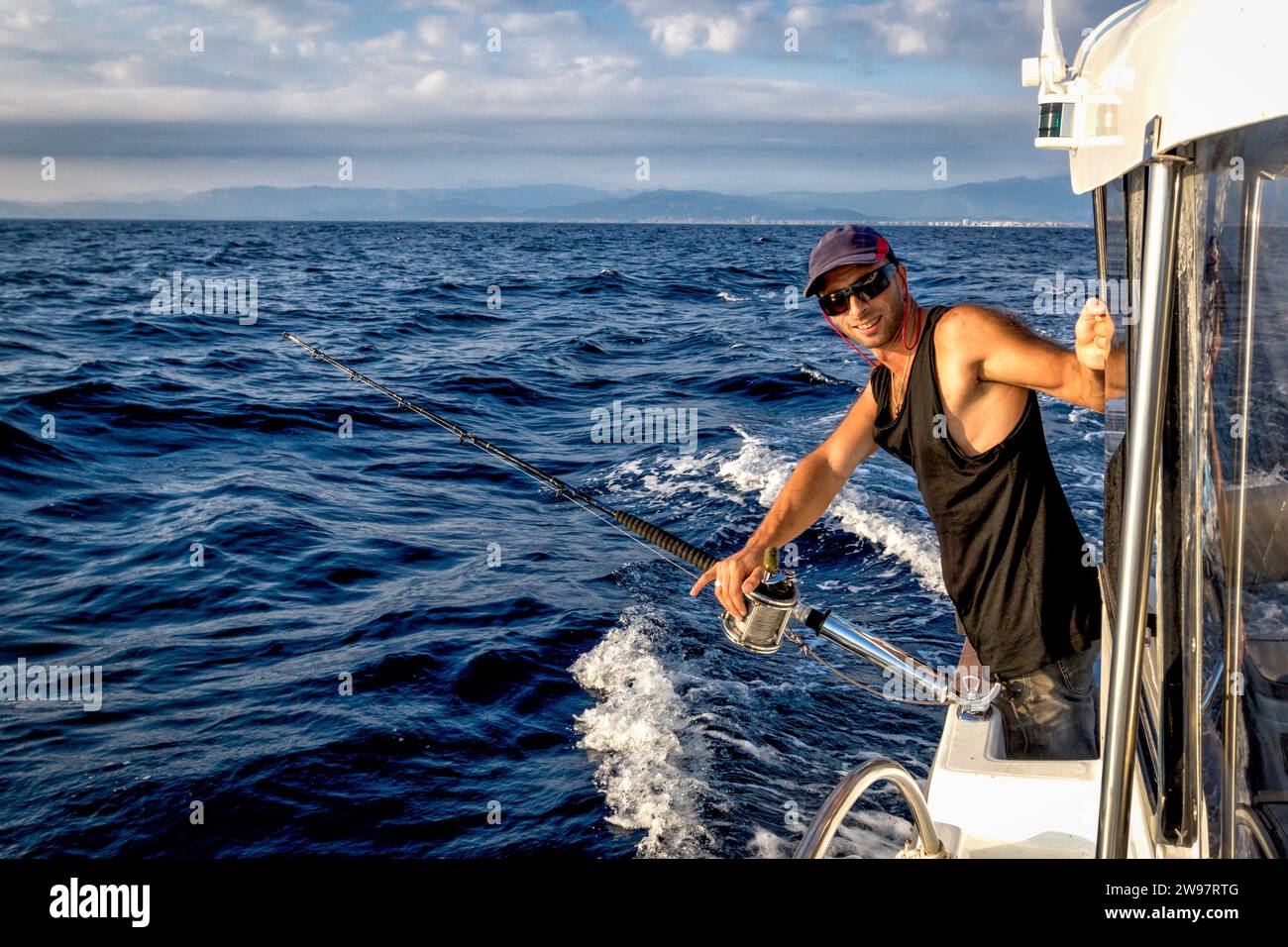 Der junge Mann in einer Baseball Cap an Bord des Schiffes im Laufe der Fischerei vor dem Hintergrund des blauen Meeres. Stockfoto