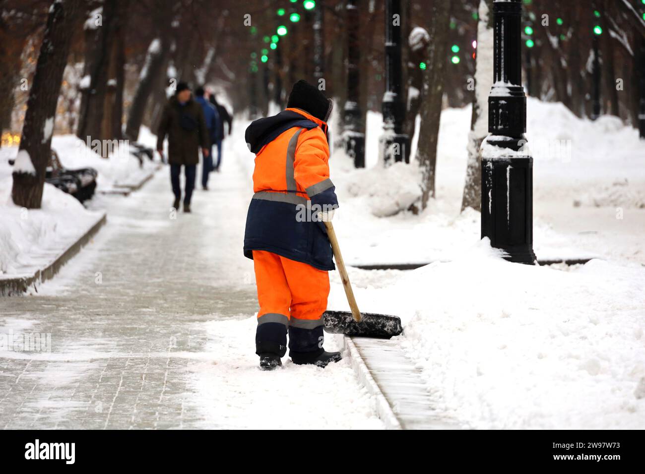 Kommunaler Arbeiter in Uniform mit Schaufel räumt Schnee auf einem Bürgersteig ab. Frau bei Schneeräumung in der Winterstadt, Straßenreinigung Stockfoto