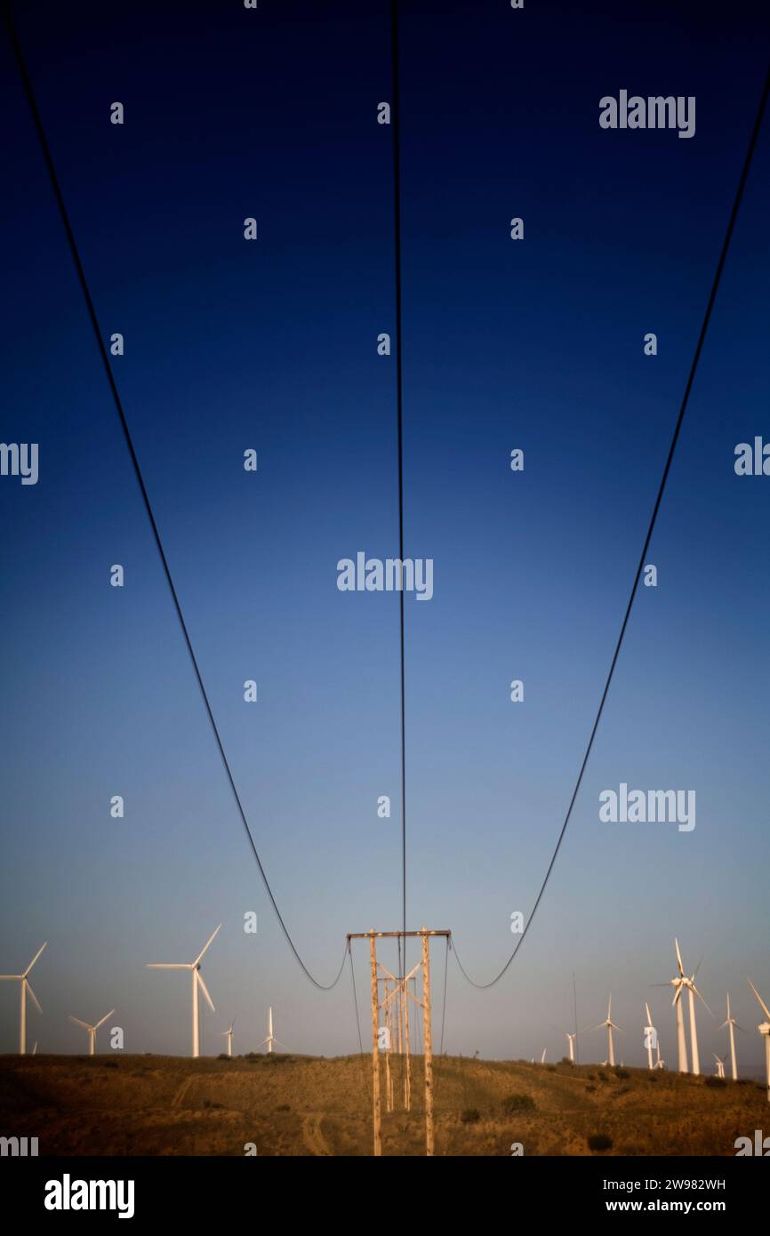 Stromleitungen führen zu einem Strompol zwischen Windmühlen. Stockfoto