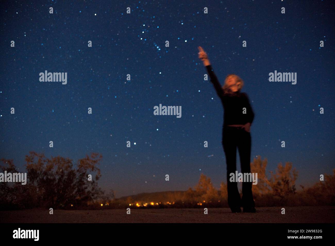 Eine Frau zeigt auf den Nachthimmel in der Wüste. (Verschwommenes Bild) Stockfoto