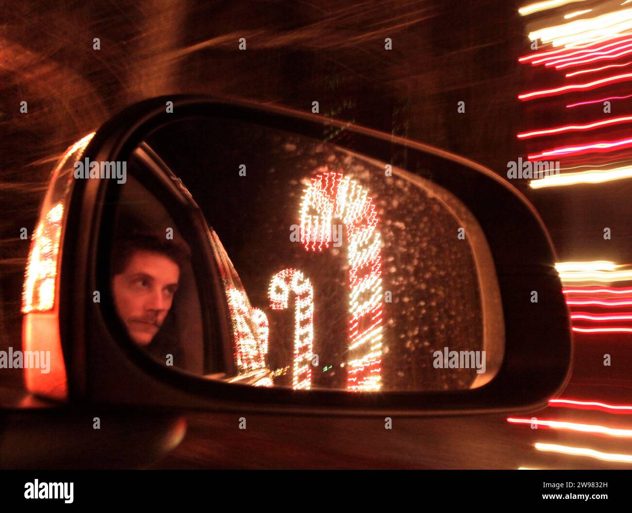 Die Reflexion eines Mannes in einem Autospiegel, vorbei an riesigen, beleuchteten Zuckerstangen. Stockfoto