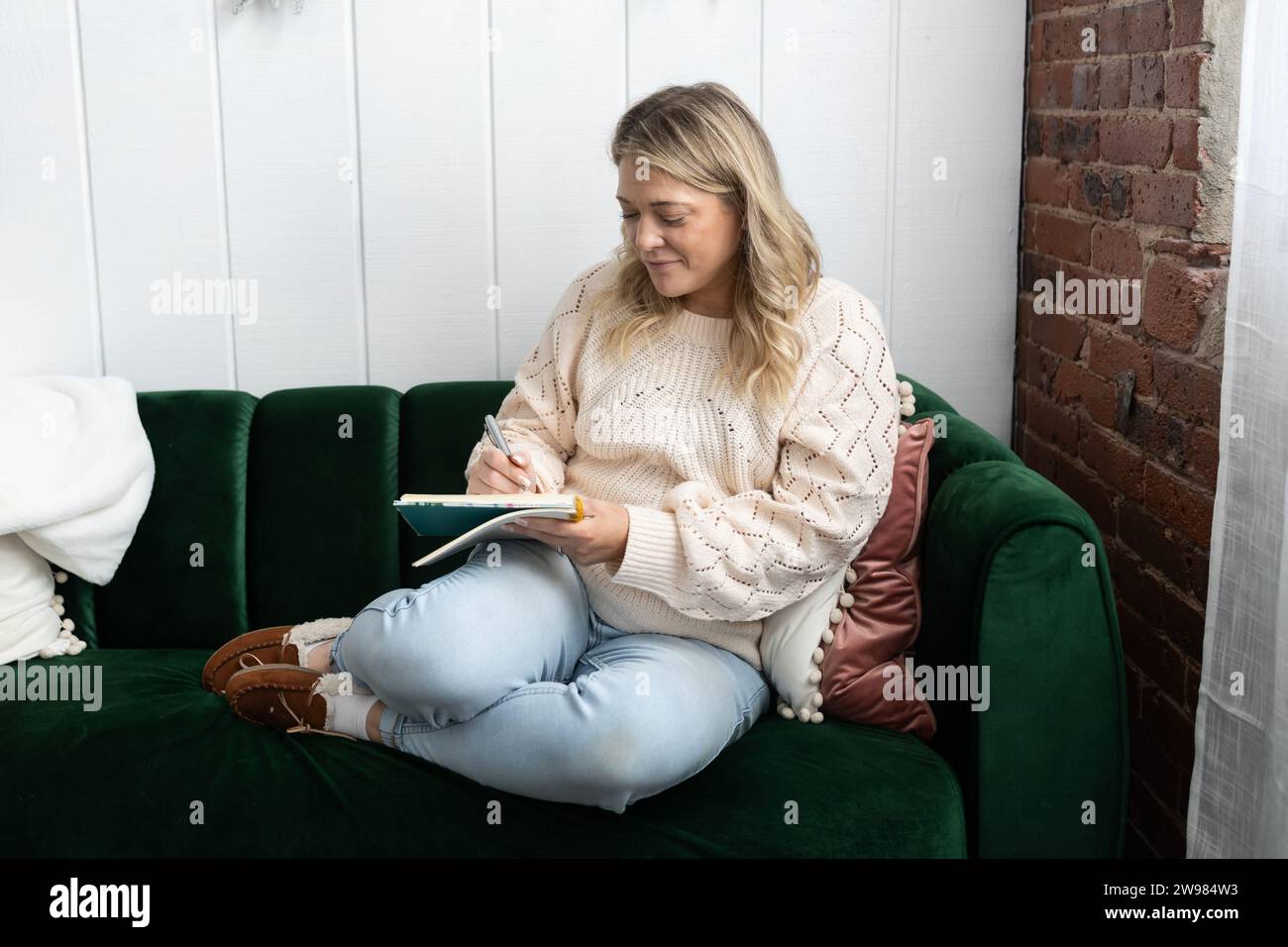 30-jährige Frau, die auf Couch sitzt und journalisiert Stockfoto