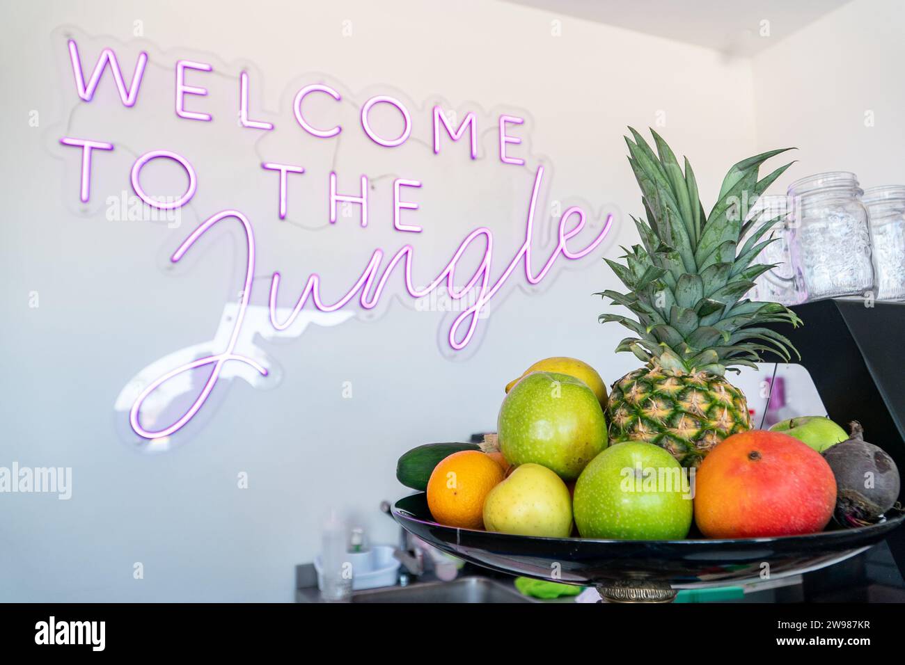 Eine Schüssel Obst vor einem Willkommensgruß im Dschungel-Neonschild Stockfoto