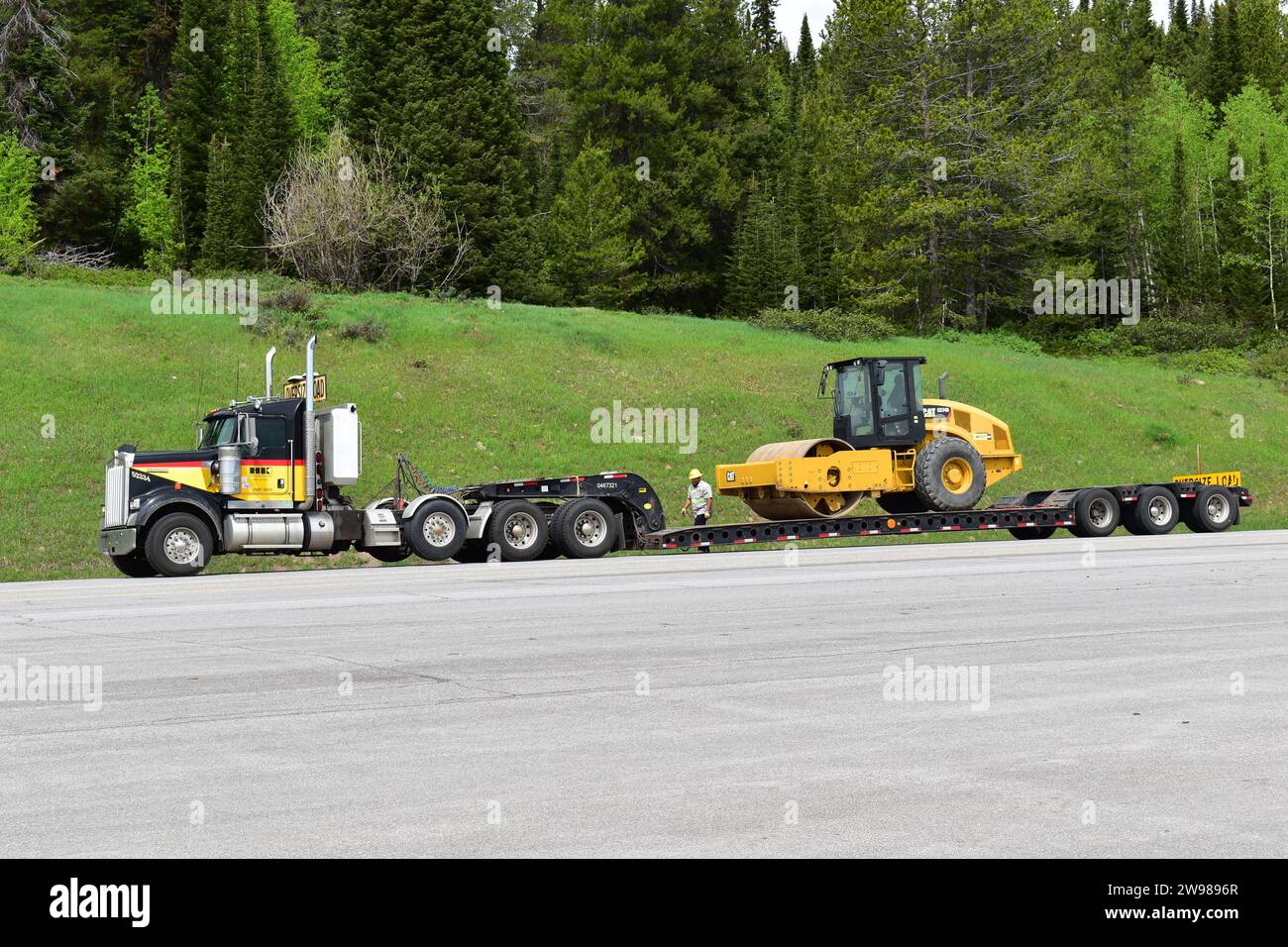 Ein Lkw mit abgesenktem Tieflader, der einen gelben CAT-Planierschild transportiert Stockfoto