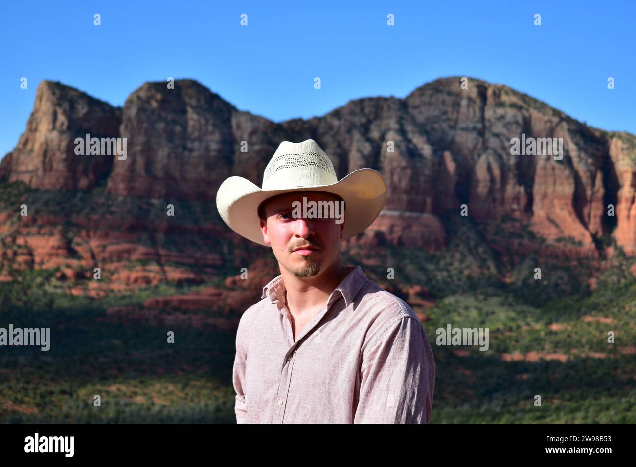 Mann in rosa Hemd und mit einem weißen Cowboyhut mit der Landschaft von Sedona in der Wüste von Arizona als Hintergrund Stockfoto