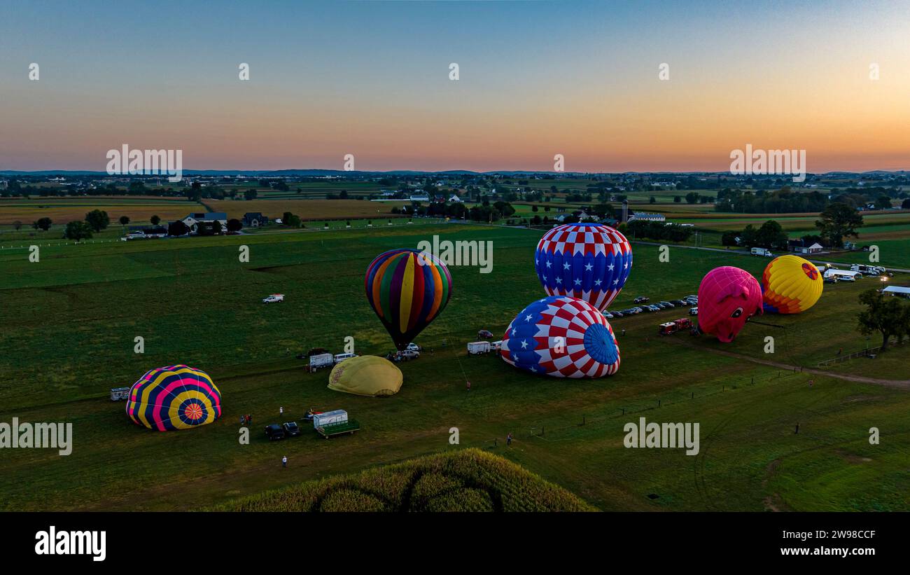 Ein Blick aus der Luft auf vielen Heißluftballons, die am frühen Morgen von einem Feld im ländlichen Amerika an einem sonnigen Sommertag starten Stockfoto