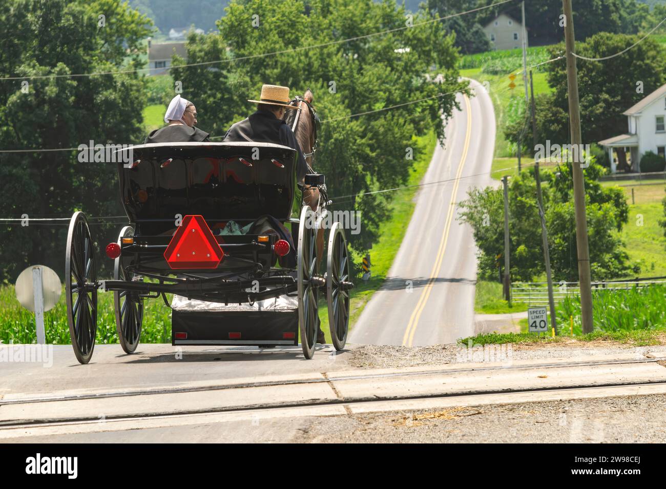 Ronks, Pennsylvania, 23. Juli 2023 - Rückansicht eines amischen Paares in einem offenen Pferd und Buggy, der an einem sonnigen Sommertag eine Landstraße entlang fährt Stockfoto