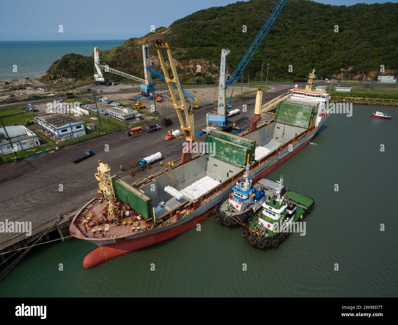 Luftaufnahme des Frachtschiffes im Hafen, das Vorräte für humanitäre Hilfe mit Kränen und großen Nahrungsmittelpaketen verlädt Stockfoto