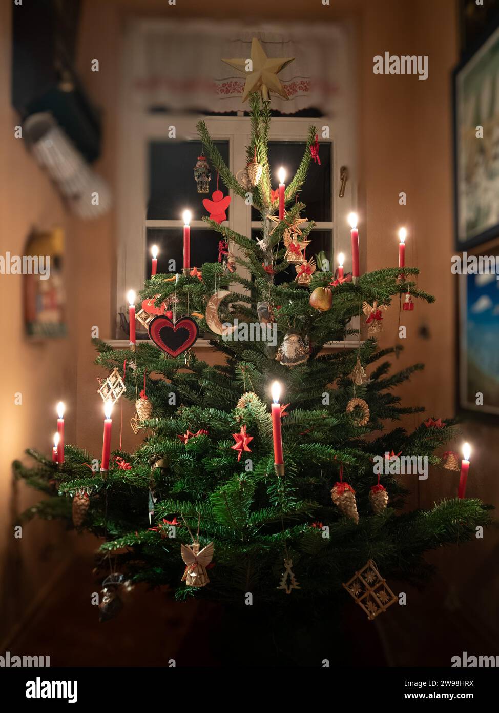 Weimar, Deutschland. Dezember 2023. In der Ecke eines Wohnzimmers steht am Heiligabend ein Weihnachtsbaum, dekoriert mit beleuchteten Kerzen und kleinen Figuren. Quelle: Soeren Stache/dpa/Alamy Live News Stockfoto