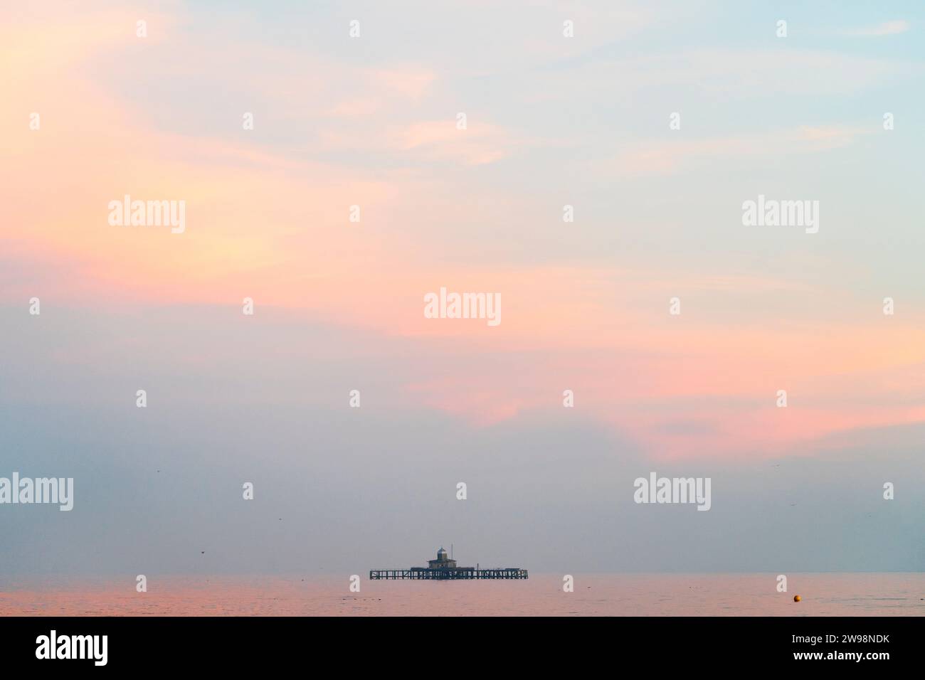 Die Ruinen der Herne Bay Pierhead, eine Meile vor der Küste im frühen Morgenlicht mit pastellfarbenen Wolken darüber und einem sehr ruhigen Meer. Stockfoto