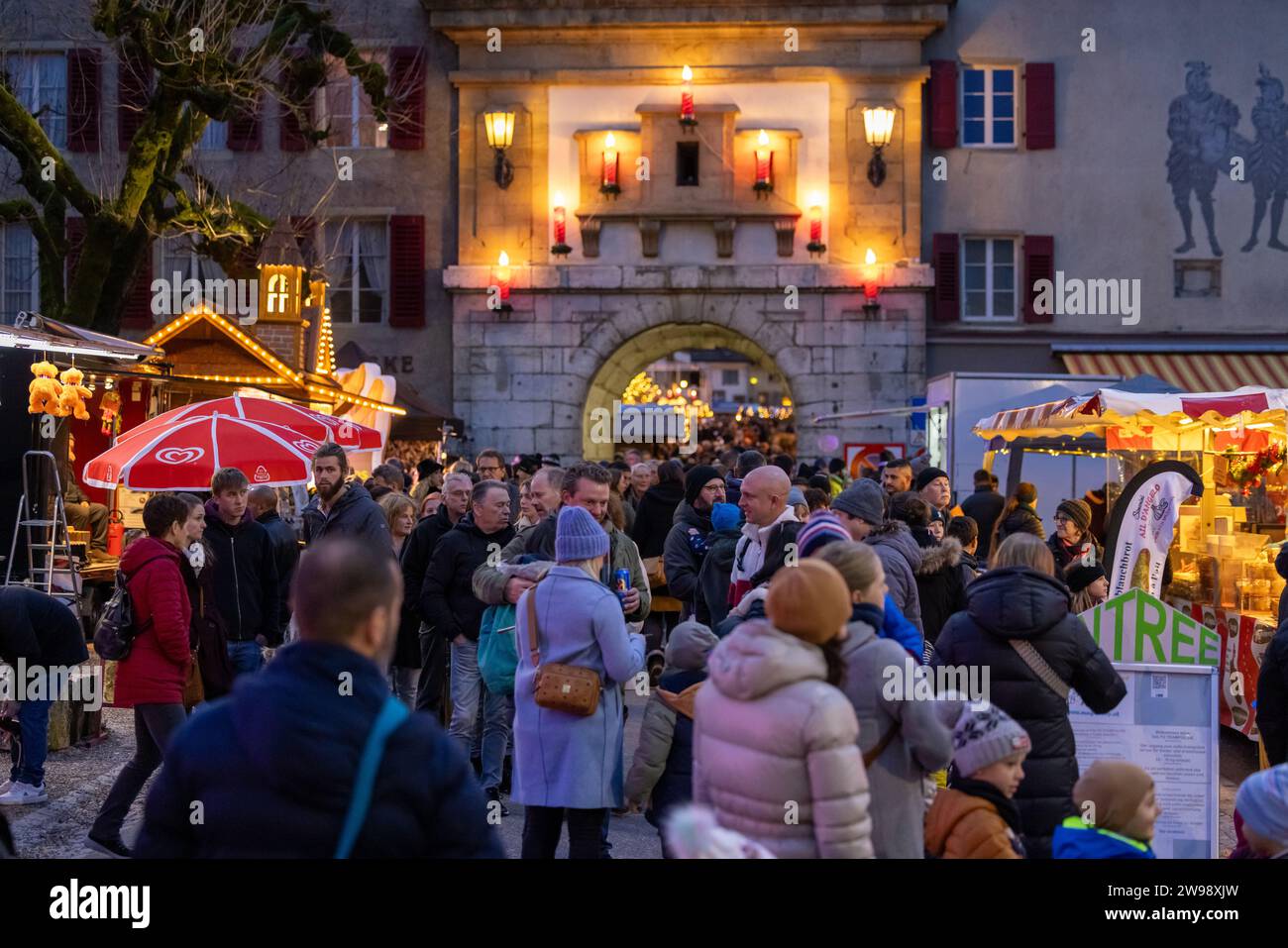 Eine lebhafte Straßenszene bei Nacht, in der die Leute an Weihnachten um die geschmückten Buden herumschleifen. Stockfoto