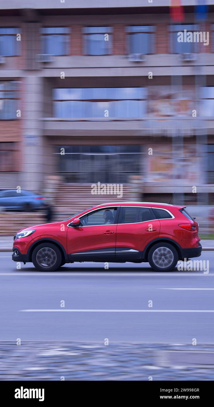 Ein modernes rotes Auto parkt mitten in einer belebten Straße, ein weiteres Auto fährt im Hintergrund vorbei Stockfoto