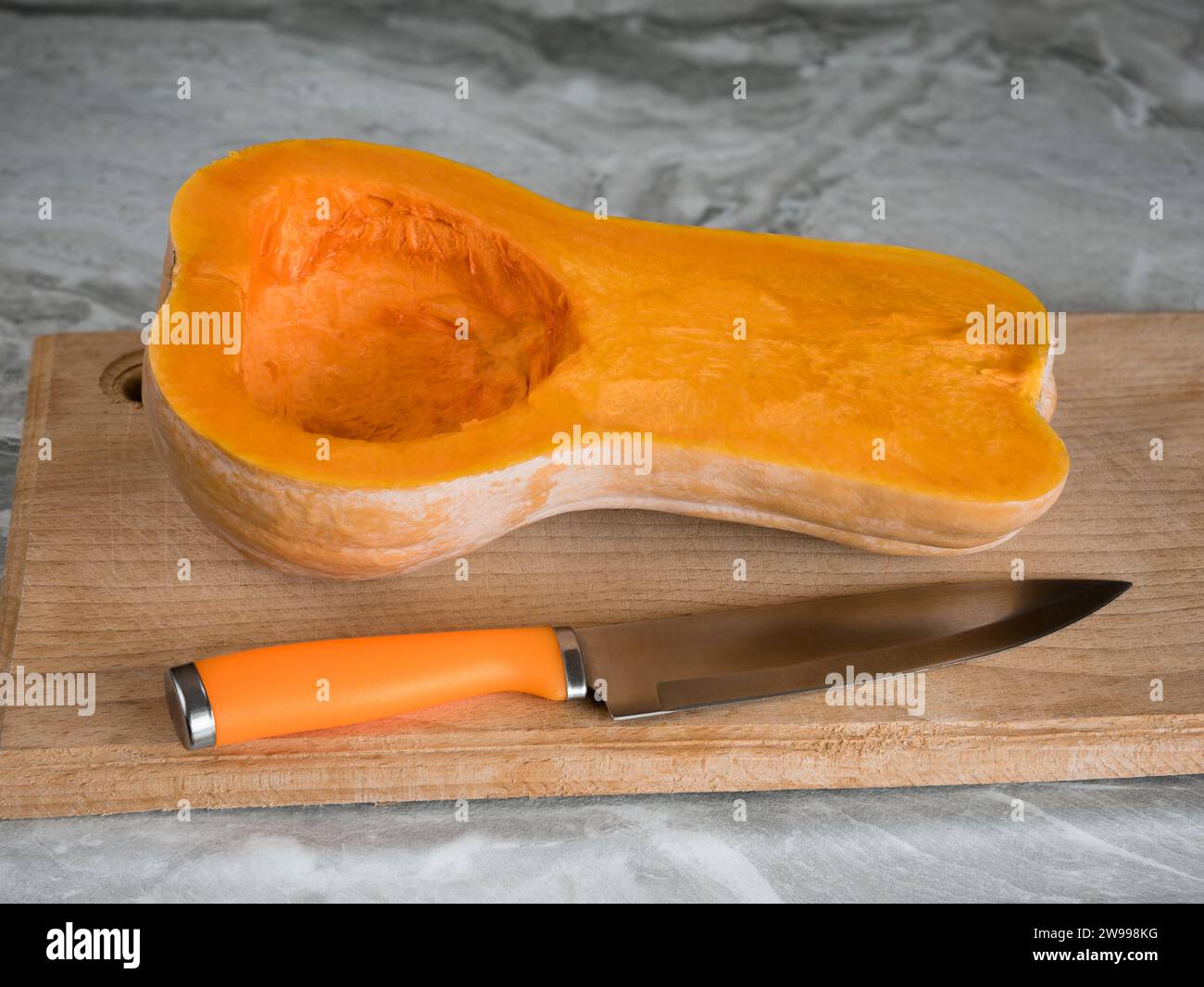 Halber Butternusskürbis (Cucurbita moschata), bekannt als Butternusskürbis oder Gramma geschnitten und mit einem Messer auf einem Schneidebrett gereinigt Stockfoto