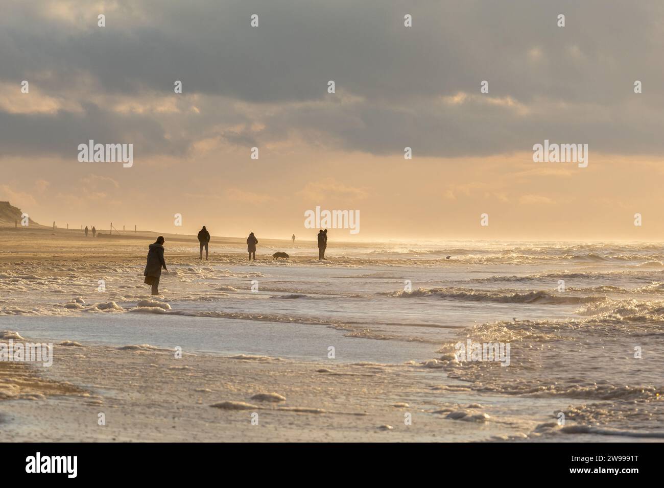 Eine Gruppe von Menschen macht einen Abendspaziergang am Strand entlang, beleuchtet von einem wunderschönen Sonnenuntergang Stockfoto