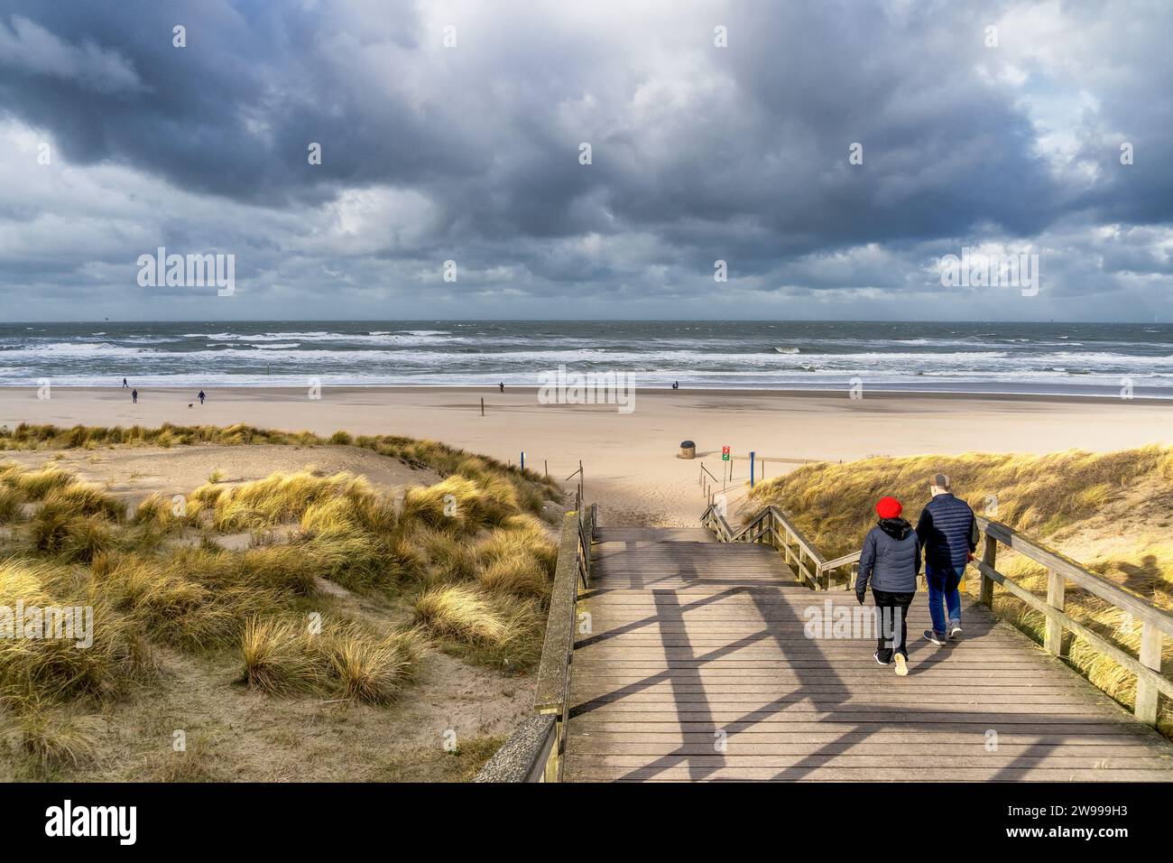 Zwei Erwachsene, die an einem bewölkten Tag in den Niederlanden Holztreppen zum Strand hinaufsteigen Stockfoto