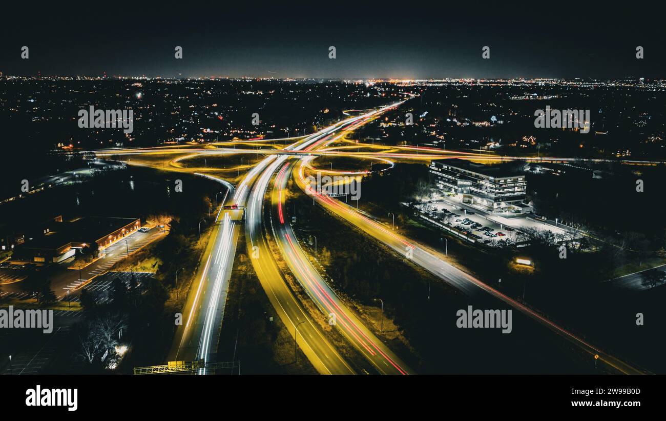 Die von Scheinwerfern beleuchteten Autos fahren über eine erhöhte Straße am Abendhimmel und schaffen so einen beeindruckenden Anblick Stockfoto