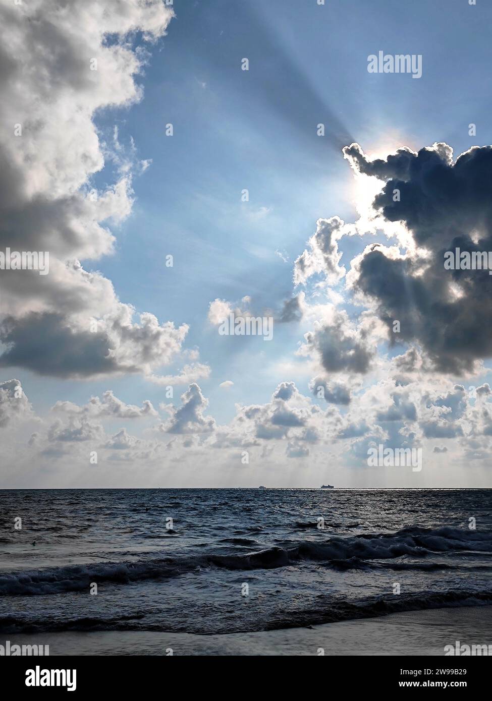 Ein ätherisches Bild eines ruhigen blauen Himmels mit einem Sonnenstrahl, der durch die Wolken strömt, beleuchtet über einem friedlichen Gewässer Stockfoto