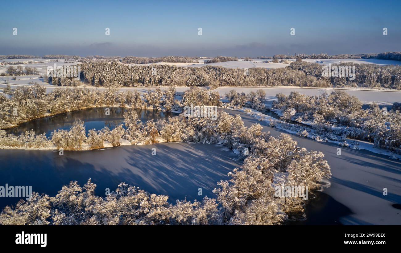 Ein Blick aus der Vogelperspektive auf schneebedeckte Bäume, die einen Fluss inmitten eines Waldes umgeben. Stockfoto