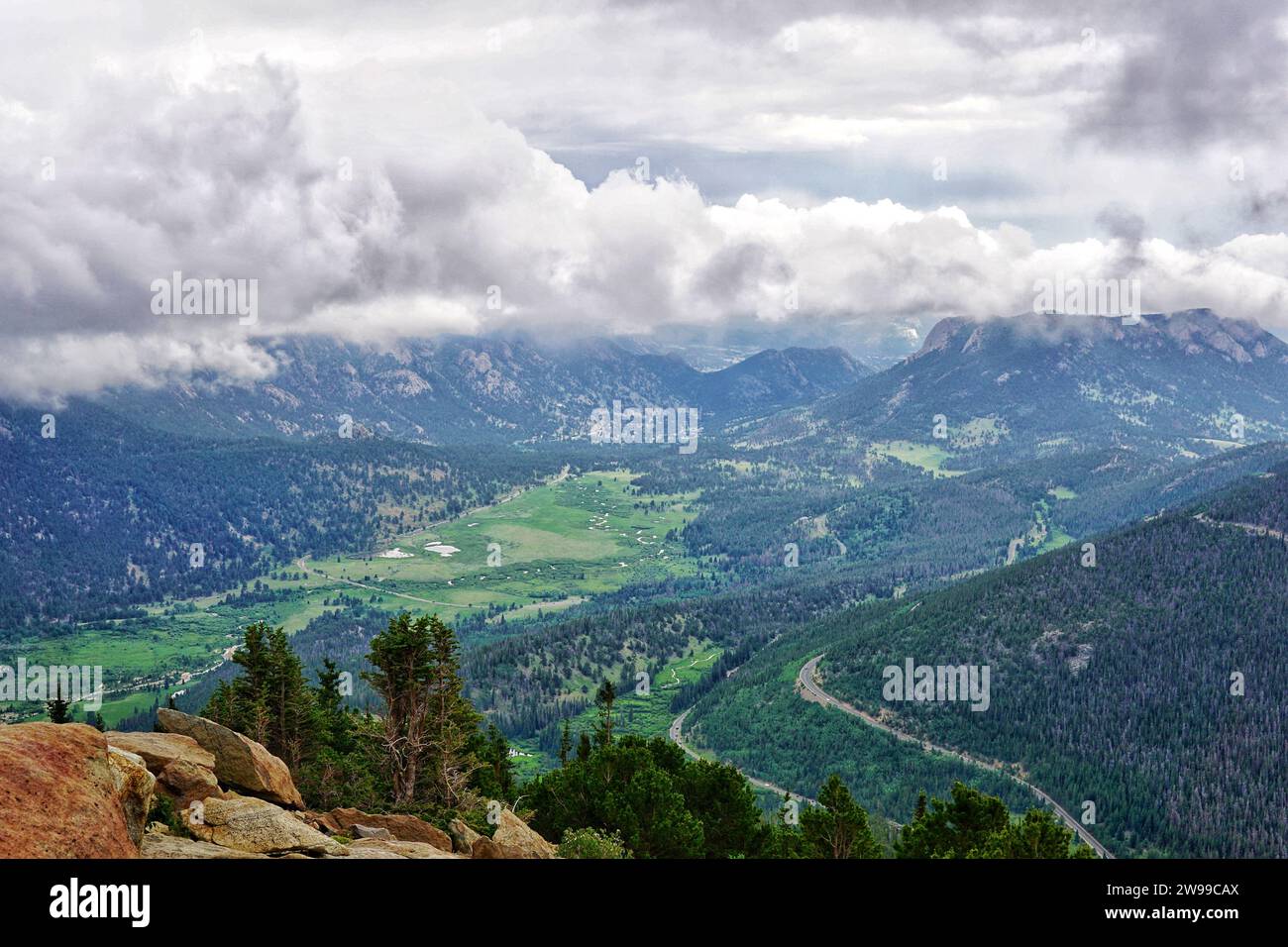 Ein Blick aus der Vogelperspektive auf ein Bergtal zeigt eine ruhige Landschaft, umgeben von üppigen grünen Hügeln und ein paar Bäumen an einem bewölkten Tag Stockfoto
