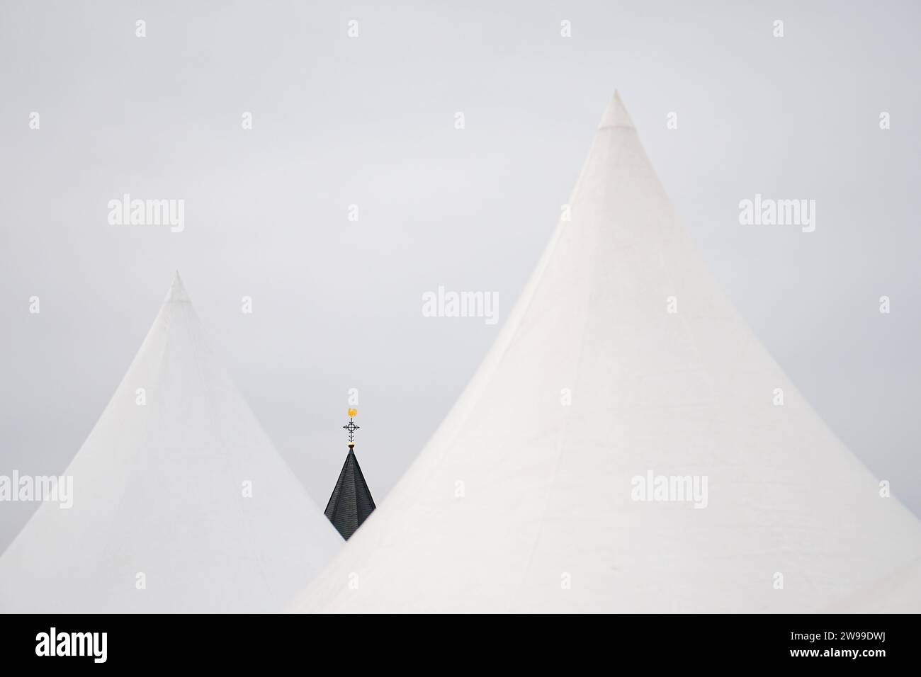 Die Spitze eines Kirchturms mit einem montierten goldenen Wetterhahn, eingerahmt von zwei weißen Zeltspitzen Stockfoto
