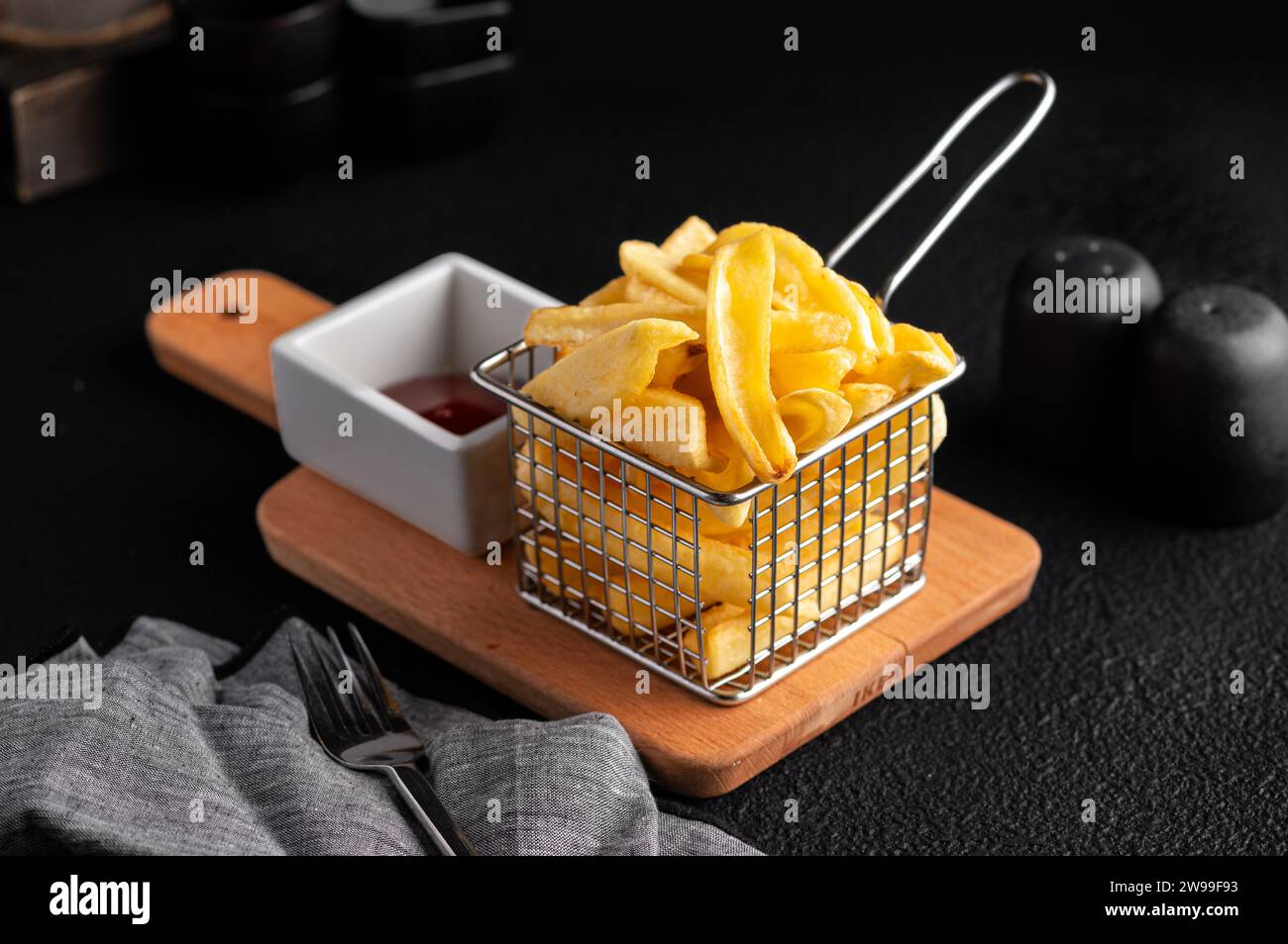 Eine herrliche Portion Pommes frites, die in einem Korb auf einem rustikalen Holzschneidebrett präsentiert werden. Stockfoto