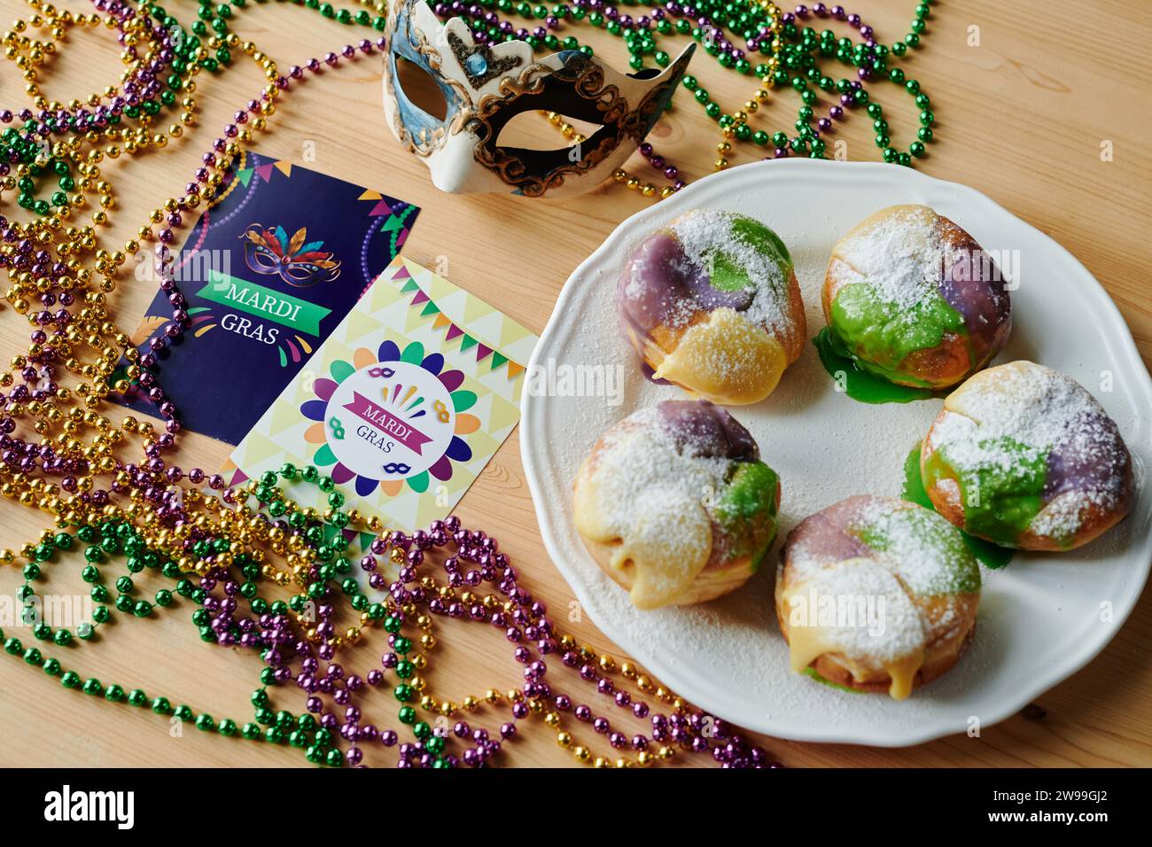 Teller mit mehreren hausgemachten berliner Donuts, die neben anderen Symbolen des Mardi Gras stehen, wie Postkarten, venezianische Maske und Perlen Stockfoto