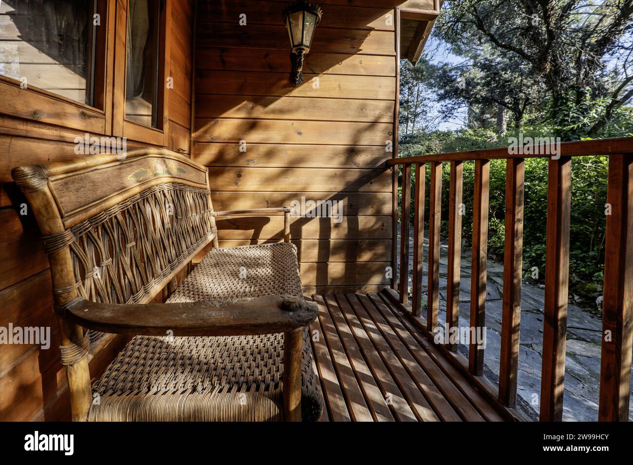 Eine Holz- und Korbbank auf der Veranda einer Blockhütte mit einem Holzgeländer Stockfoto