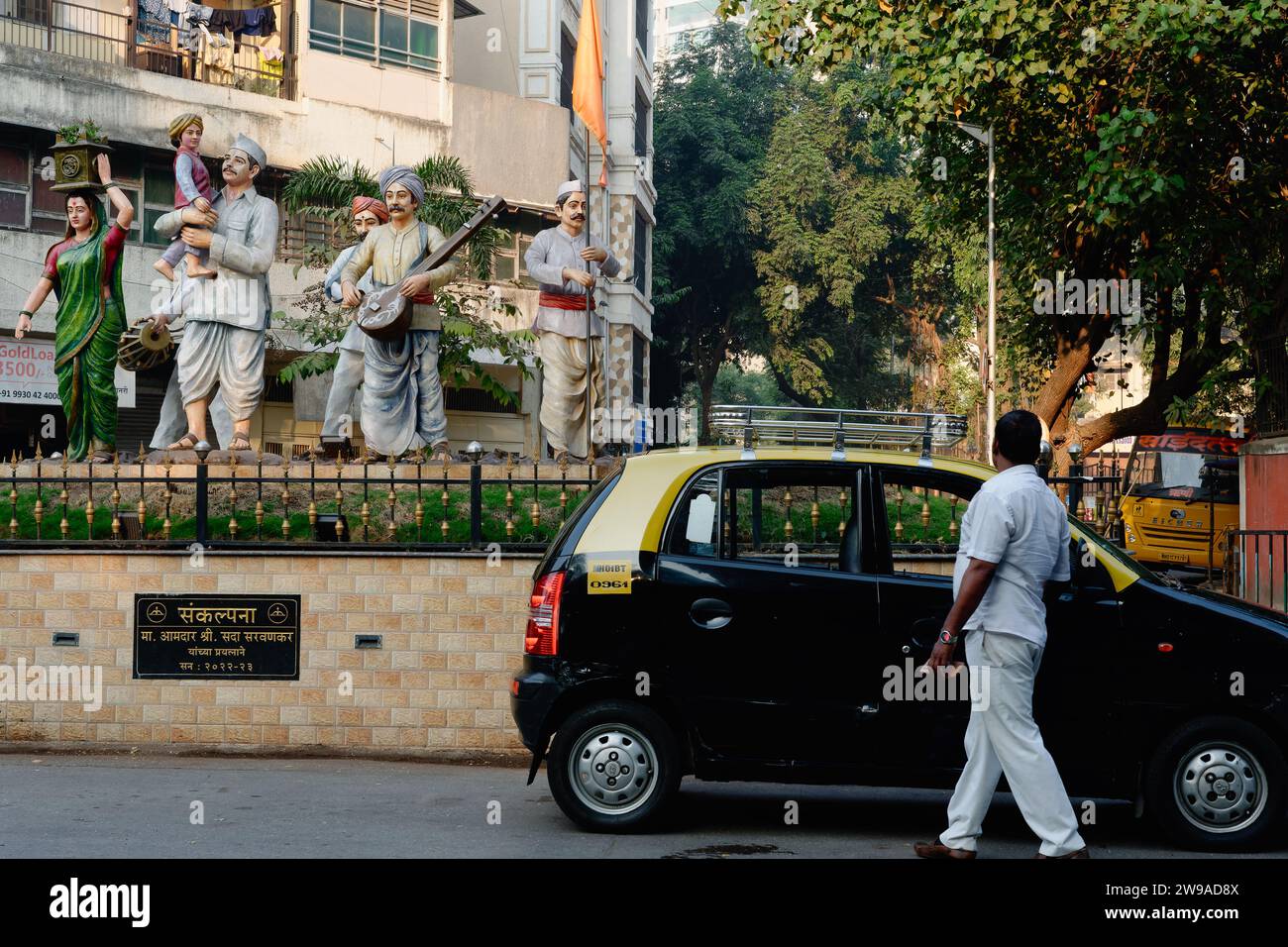 Statuen in Dadar, Mumbai, Indien, die Maharashtrian Dorfbewohner während einer religiösen Prozession darstellen; rechts: Ein typisches schwarz-gelbes Mumbai Taxi Stockfoto