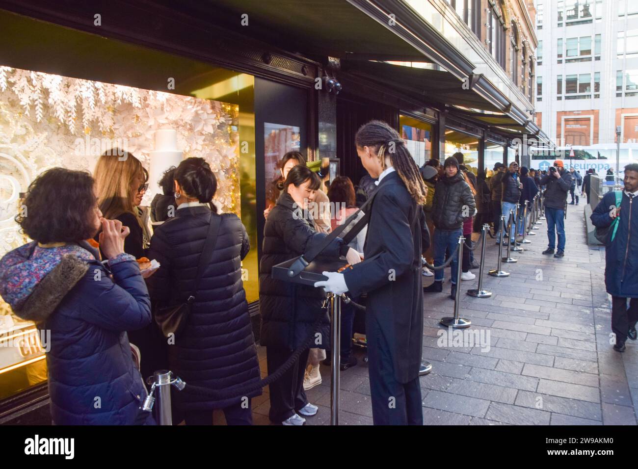 London, Großbritannien. Dezember 2023. Die Mitarbeiter servieren Gebäck und heiße Getränke, während die Gäste vor Harrods in Knightsbridge für das Angebot am zweiten Weihnachtsfeiertag anstehen. Quelle: Vuk Valcic/Alamy Live News Stockfoto